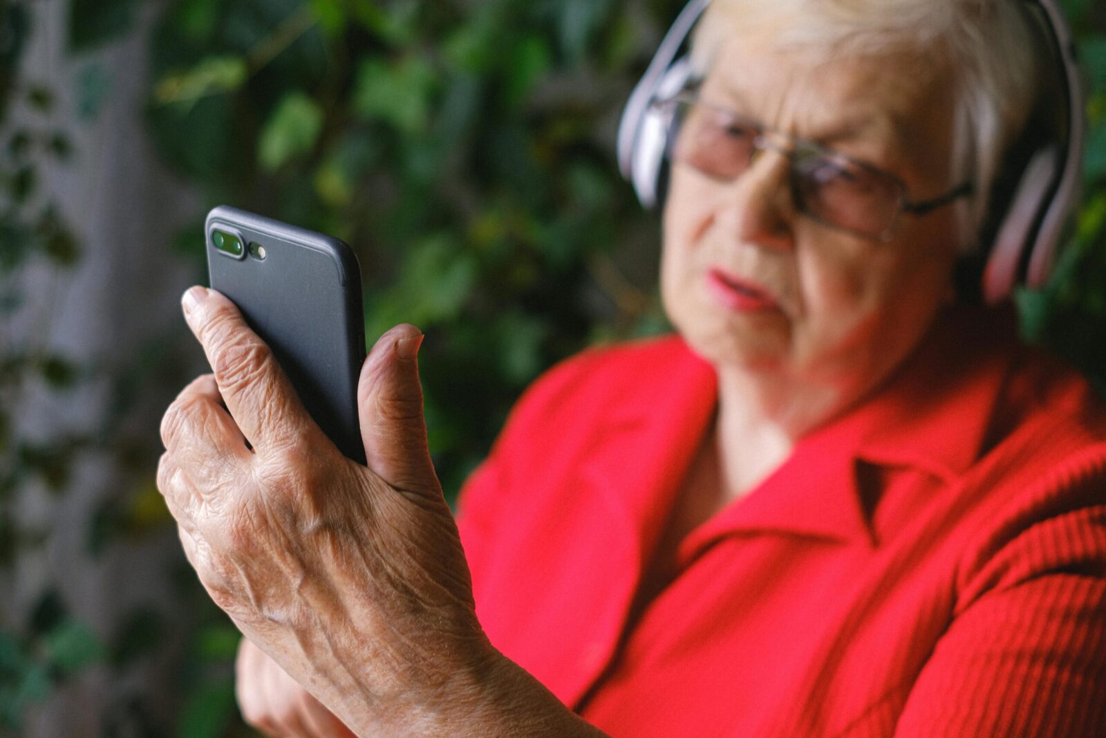 Senior woman in red using smartphone with headphones outdoors.